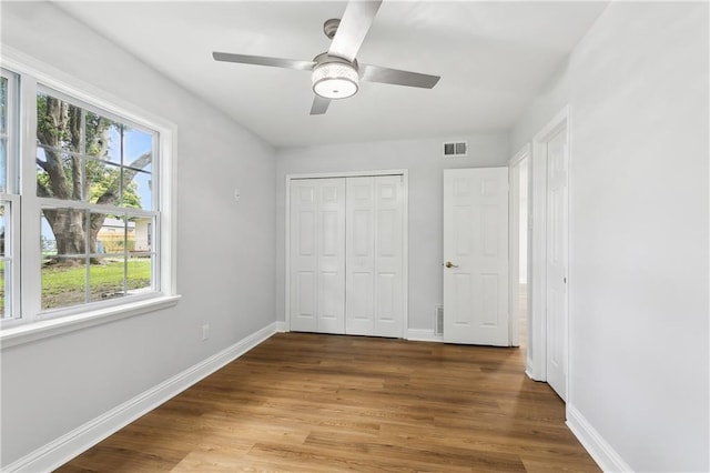 unfurnished bedroom featuring multiple windows, ceiling fan, hardwood / wood-style floors, and a closet