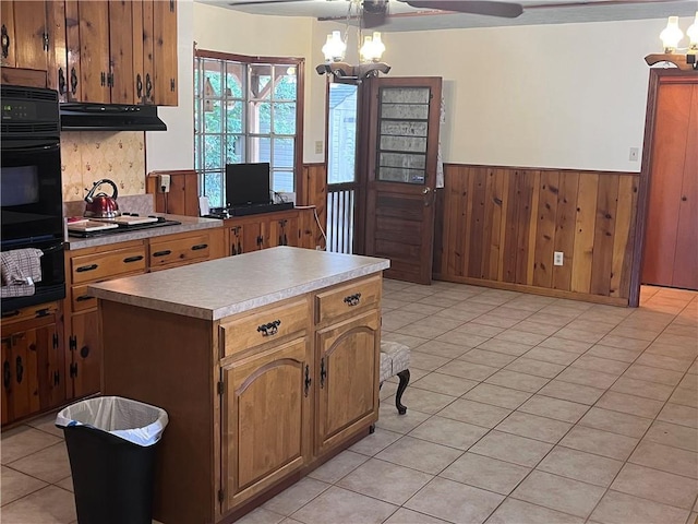 kitchen with wooden walls, a center island, light tile patterned floors, gas cooktop, and ceiling fan