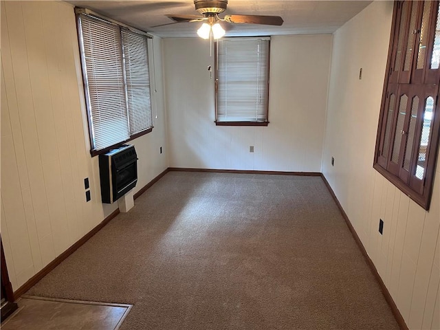 spare room with ceiling fan, wooden walls, heating unit, and dark colored carpet