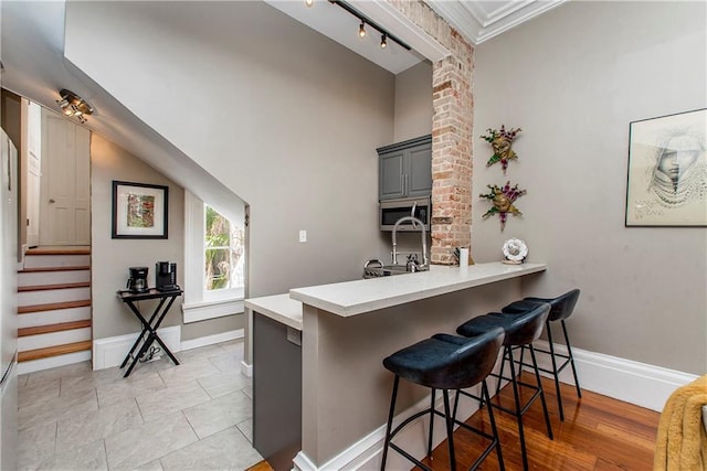 kitchen featuring ornamental molding, gray cabinetry, a kitchen bar, and kitchen peninsula