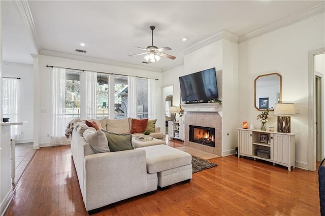 living room featuring a tile fireplace, wood-type flooring, ceiling fan, and crown molding