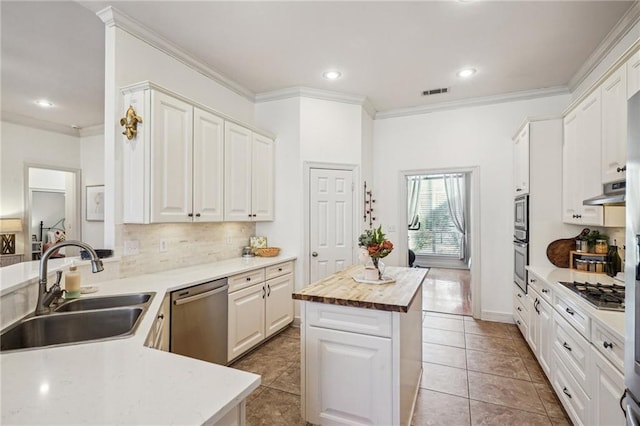 kitchen with sink, wooden counters, appliances with stainless steel finishes, white cabinetry, and a center island