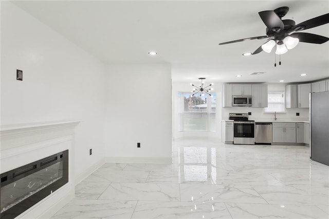 kitchen with stainless steel appliances, baseboards, marble finish floor, gray cabinets, and a glass covered fireplace