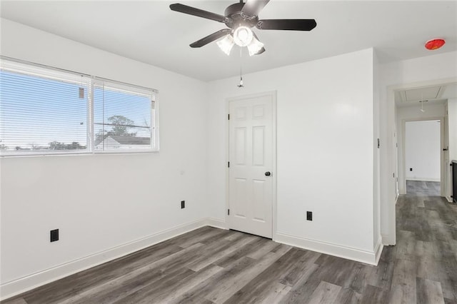 empty room featuring attic access, baseboards, dark wood finished floors, and a ceiling fan