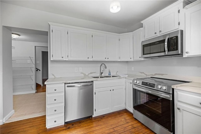 kitchen with sink, stainless steel appliances, light hardwood / wood-style floors, light stone countertops, and white cabinets