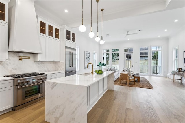 kitchen with an island with sink, sink, custom exhaust hood, high end appliances, and light stone counters