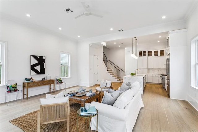 living room featuring ceiling fan, ornamental molding, sink, and light hardwood / wood-style floors