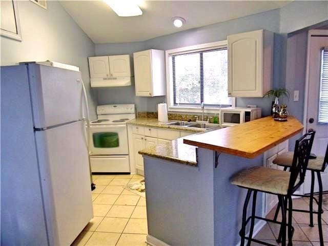 kitchen with light tile patterned flooring, sink, a breakfast bar area, white appliances, and white cabinets