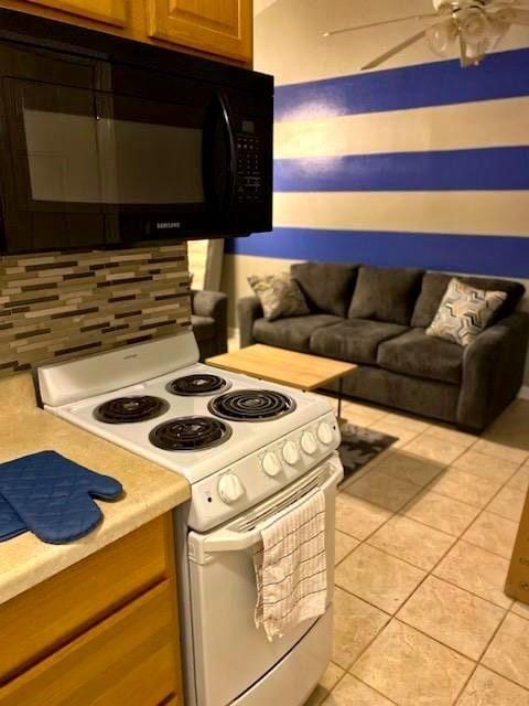 kitchen with light tile patterned flooring, ceiling fan, white electric stove, and tasteful backsplash