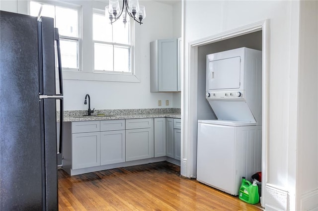 laundry room featuring stacked washing maching and dryer, laundry area, an inviting chandelier, a sink, and light wood-style floors