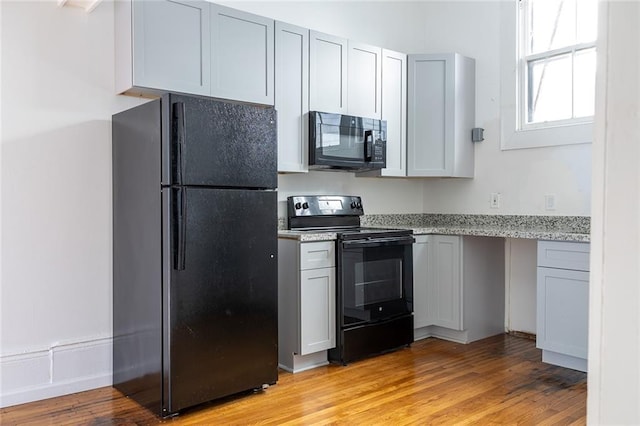 kitchen featuring light stone countertops, black appliances, and light wood-style flooring