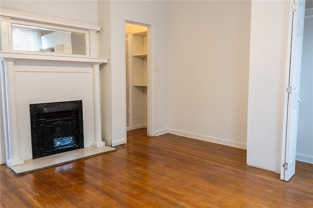 unfurnished living room with baseboards, a fireplace with raised hearth, and wood finished floors