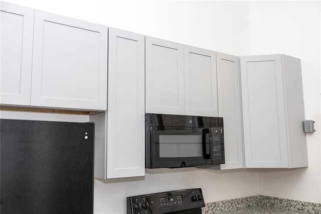 interior details featuring stove, white cabinets, black microwave, and light countertops