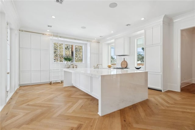 kitchen featuring white cabinetry, light parquet flooring, and a center island with sink