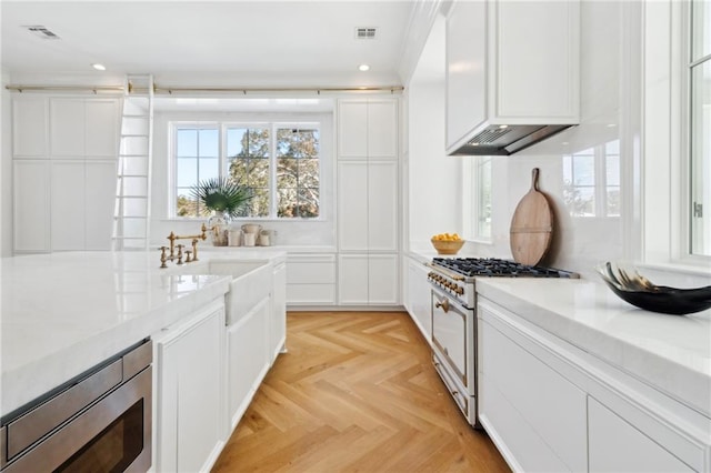 kitchen featuring sink, white cabinetry, high end range, stainless steel microwave, and light parquet floors