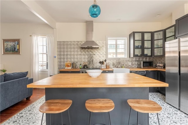 kitchen featuring sink, stainless steel refrigerator, backsplash, a kitchen bar, and wall chimney exhaust hood