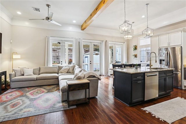 kitchen featuring appliances with stainless steel finishes, beamed ceiling, white cabinets, light stone countertops, and a center island with sink