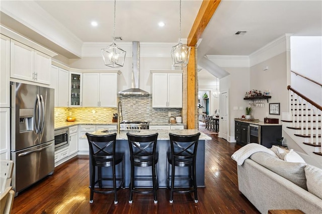 kitchen with a breakfast bar, appliances with stainless steel finishes, white cabinetry, light stone counters, and wall chimney exhaust hood