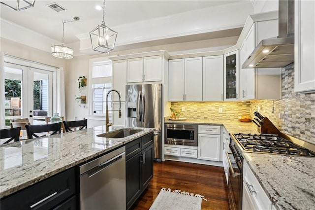 kitchen featuring wall chimney exhaust hood, sink, white cabinetry, hanging light fixtures, and stainless steel appliances