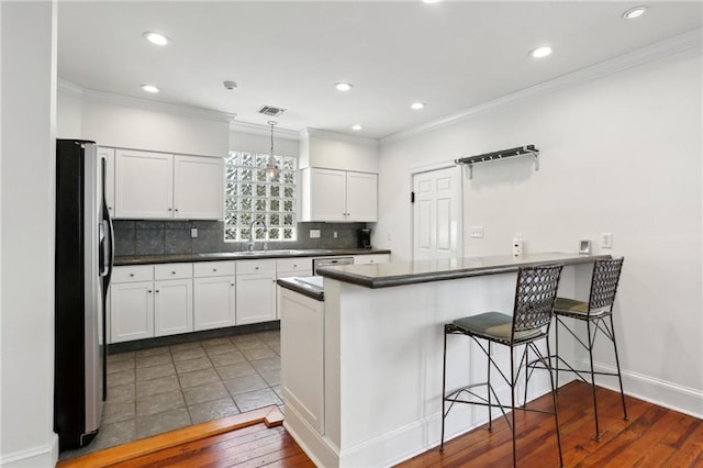 kitchen featuring a breakfast bar area, stainless steel appliances, white cabinets, decorative light fixtures, and kitchen peninsula