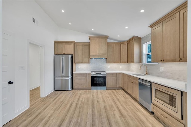 kitchen with appliances with stainless steel finishes, lofted ceiling, sink, decorative backsplash, and light wood-type flooring