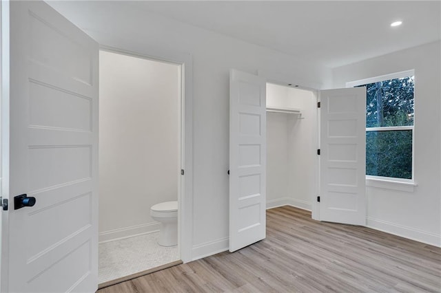 unfurnished bedroom featuring ensuite bath, a closet, and light wood-type flooring