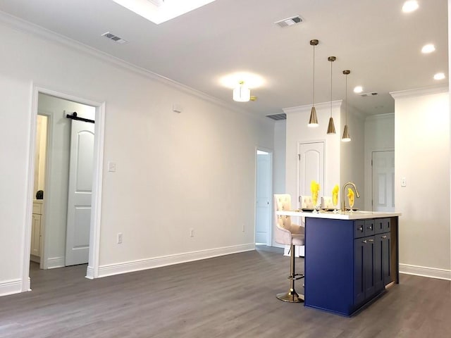 kitchen featuring dark wood-type flooring, decorative light fixtures, ornamental molding, a kitchen breakfast bar, and an island with sink