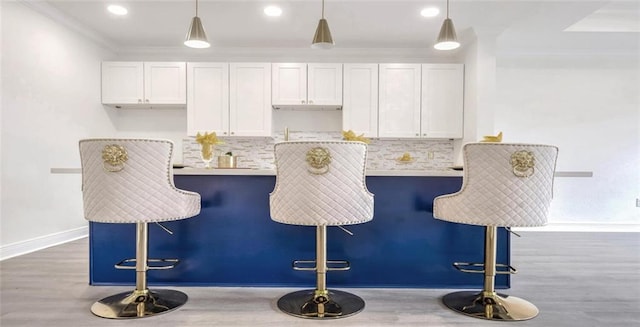 kitchen featuring pendant lighting, backsplash, a kitchen breakfast bar, and white cabinets