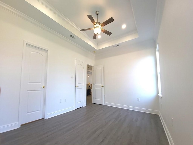 unfurnished bedroom with crown molding, ceiling fan, a tray ceiling, and dark wood-type flooring