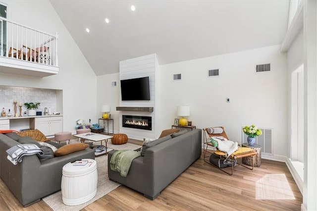 living room featuring a glass covered fireplace, visible vents, light wood finished floors, and high vaulted ceiling