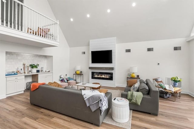 living area featuring light wood-type flooring, visible vents, and a glass covered fireplace