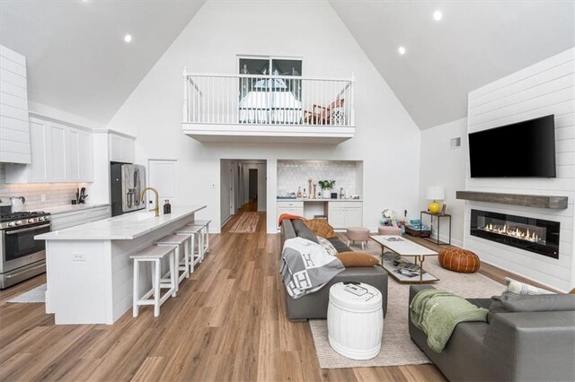 living area featuring light wood-type flooring, baseboards, high vaulted ceiling, and a glass covered fireplace