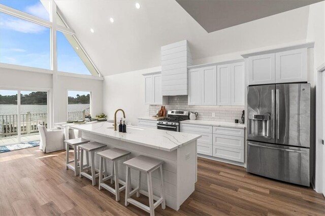 kitchen featuring light stone countertops, an island with sink, appliances with stainless steel finishes, dark wood-style floors, and a sink