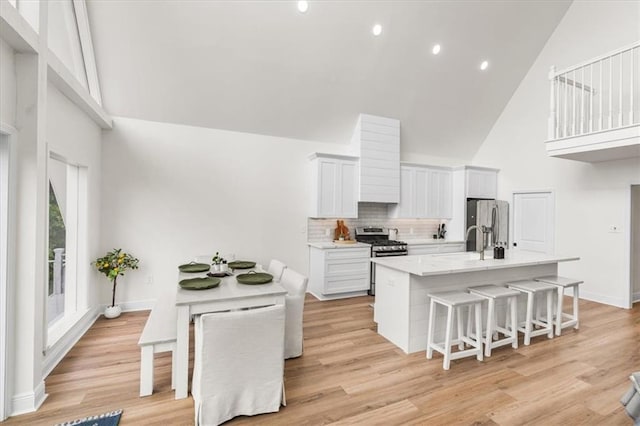 kitchen featuring high vaulted ceiling, an island with sink, light wood-style floors, appliances with stainless steel finishes, and a breakfast bar area