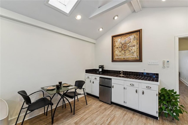 kitchen featuring lofted ceiling with skylight, white cabinetry, tile countertops, recessed lighting, and light wood finished floors