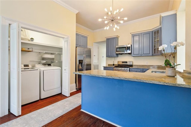 kitchen featuring pendant lighting, crown molding, dark wood-type flooring, appliances with stainless steel finishes, and washing machine and dryer