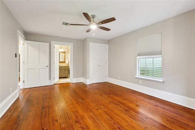 unfurnished bedroom featuring ceiling fan, ensuite bath, hardwood / wood-style floors, and a closet