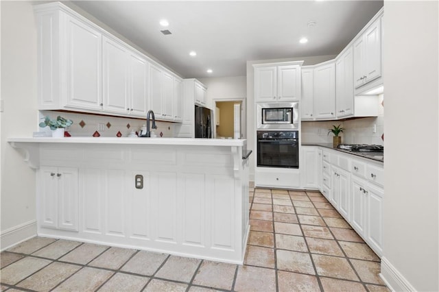 kitchen with tasteful backsplash, kitchen peninsula, white cabinets, and appliances with stainless steel finishes