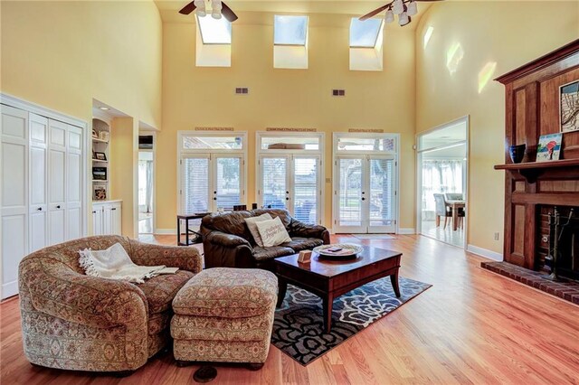 living room featuring french doors, built in shelves, a towering ceiling, ceiling fan, and light hardwood / wood-style floors