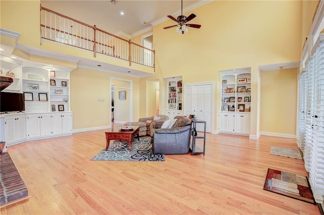 living room featuring ornamental molding, a towering ceiling, light wood-type flooring, and built in shelves