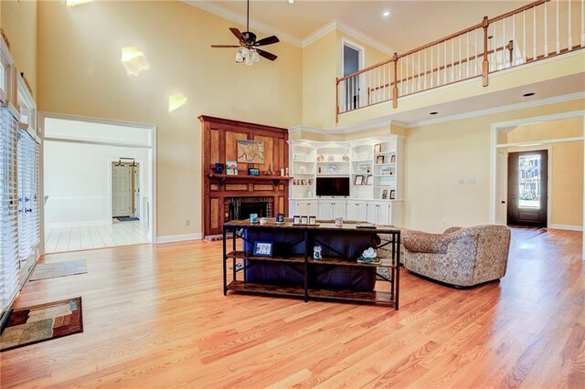 living room with crown molding, light hardwood / wood-style flooring, ceiling fan, a towering ceiling, and a fireplace