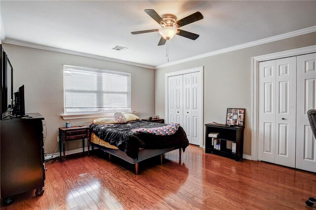 bedroom with ceiling fan, ornamental molding, hardwood / wood-style floors, and two closets