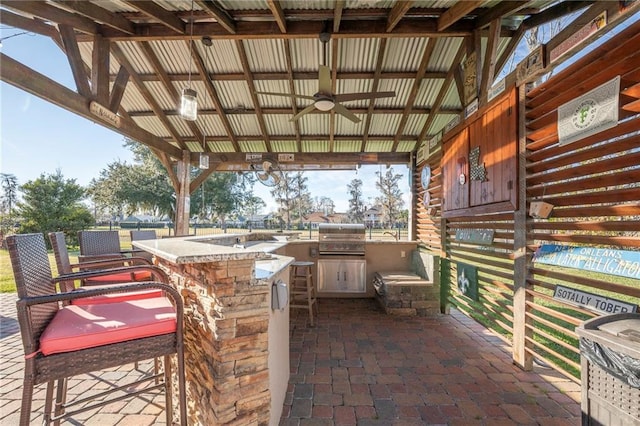 view of patio featuring a gazebo, area for grilling, a bar, ceiling fan, and exterior kitchen