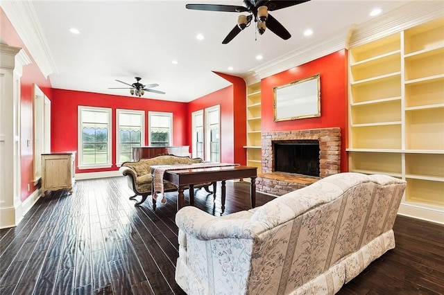 living room featuring built in shelves, ornate columns, crown molding, a brick fireplace, and dark hardwood / wood-style flooring