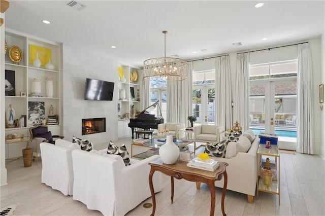 living room with a tile fireplace, an inviting chandelier, built in features, and light hardwood / wood-style floors