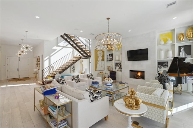 living room featuring light wood-type flooring, a large fireplace, a chandelier, and built in shelves