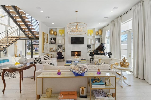 living room featuring a large fireplace, a chandelier, light hardwood / wood-style floors, and built in shelves