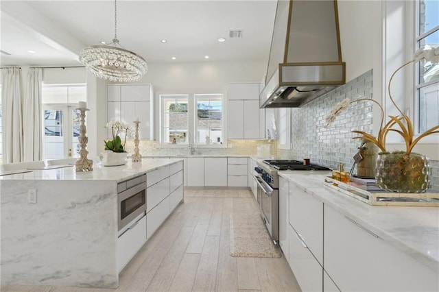 kitchen with custom exhaust hood, light stone counters, appliances with stainless steel finishes, white cabinets, and backsplash