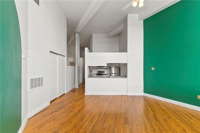 unfurnished living room featuring a high ceiling, ceiling fan, and light wood-type flooring