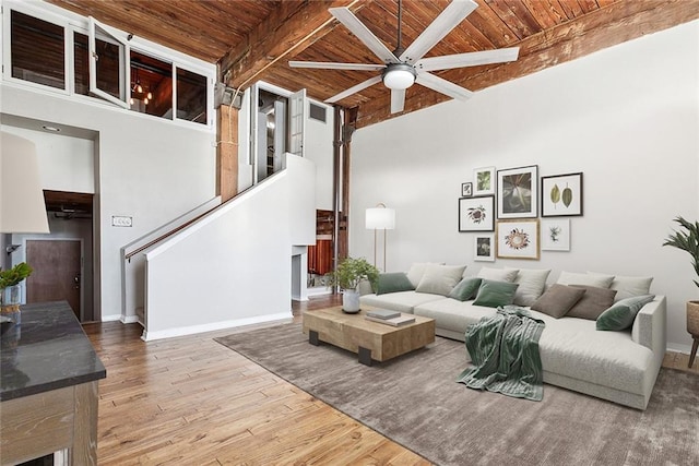 living room with a towering ceiling, hardwood / wood-style floors, ceiling fan, wood ceiling, and beam ceiling